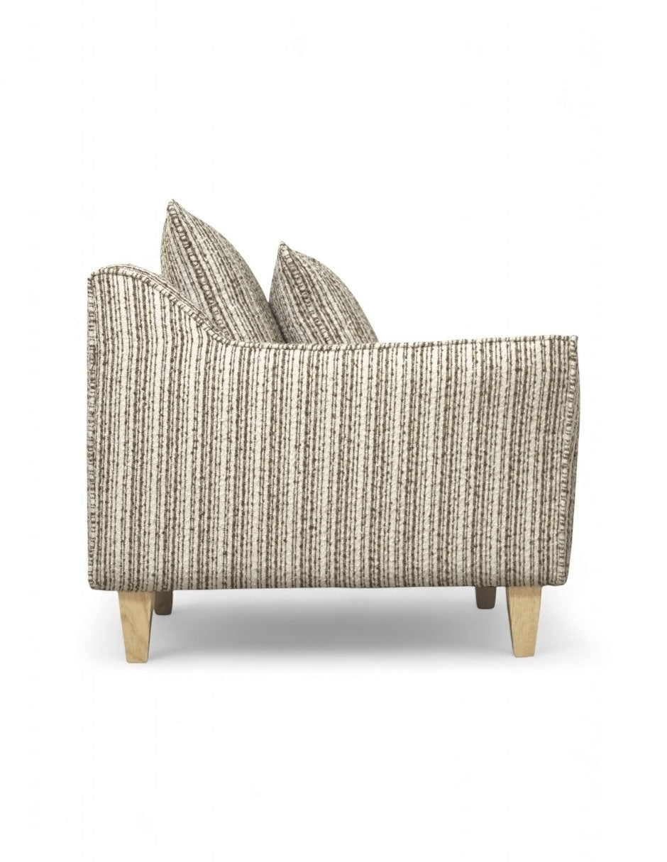 Vista lateral sillón beige de tela texturizada con diseño moderno, cojín de respaldo suelto, cojín decorativo rectangular y patas de madera natural