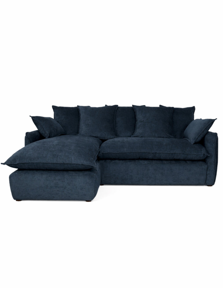 Vista frontal sofá en L azul oscuro moderno con chaise izquierdo, cojines amplios tipo almohadón 